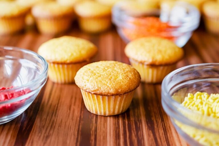 Three Mini Cupcakes Next to Glass Bowls of Red and Yellow Sprinkles