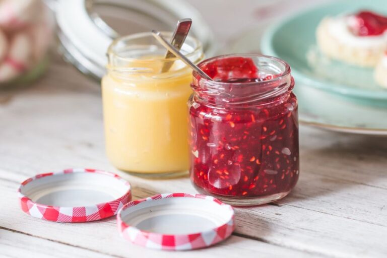 Two Jars With Lemon Curd and Raspberry Jam on a Wooden Table