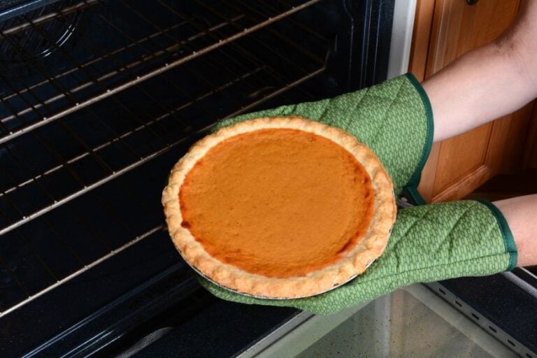 Closeup of a Woman Taking a Pumpkin Pie Out of the Oven