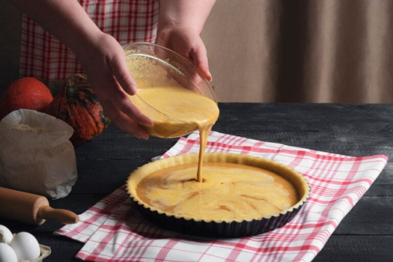 Woman Pouring Unbaked Pumpkin Pie Filling in a Crust in a Tart Pan