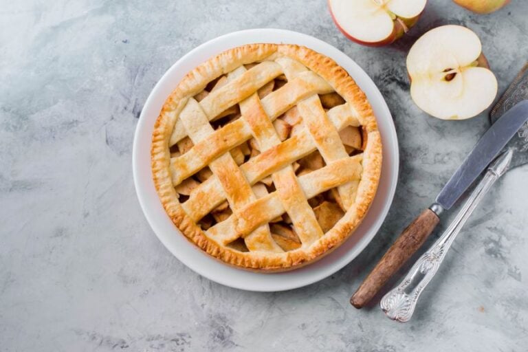 Lattice Crust Apple Pie on a White Plate With Serving Utensils and Apples